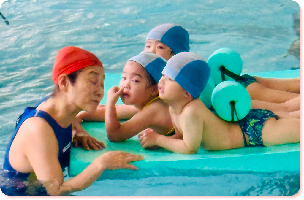 アクティビティのスイミングでプールに浮かべた大きなスポンジマットの上で浮遊を楽しむ園児たち